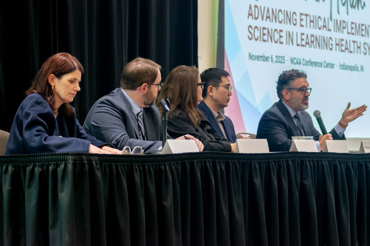 six panel members seated at a table on stage