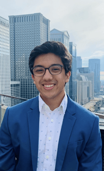 Sabin Karki, in blue blazer, wearing glasses, outside with urban skyscrapers in background