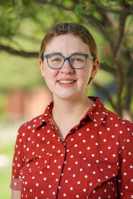 Sarah Vaught, young white woman wearing blue rimmed glasses and a rust-colored, polka dot shirt