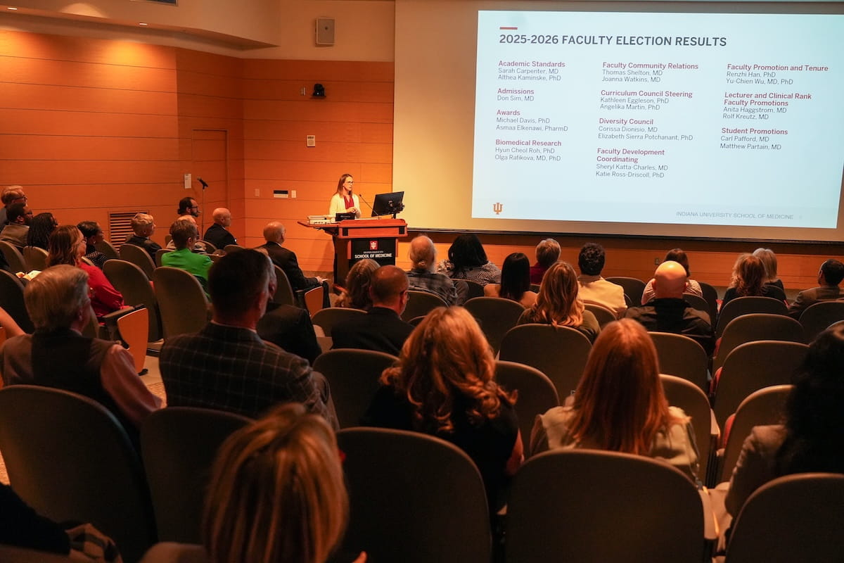 Ashley Inman stands at podium announcing results of the 2025 faculty elections.