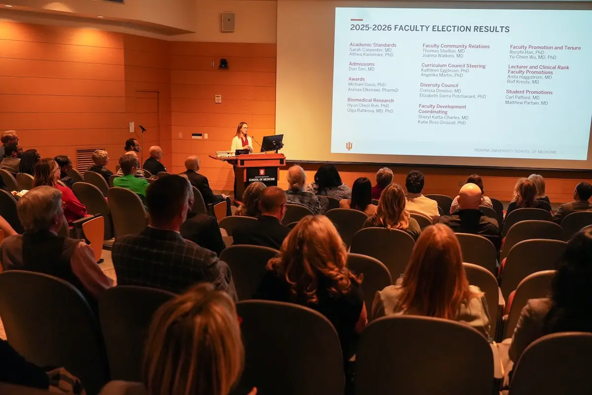 Ashley Inman stands at podium announcing results of the 2025 faculty elections.