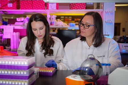 Two female researchers in the Tansey Lab work with test tubes.
