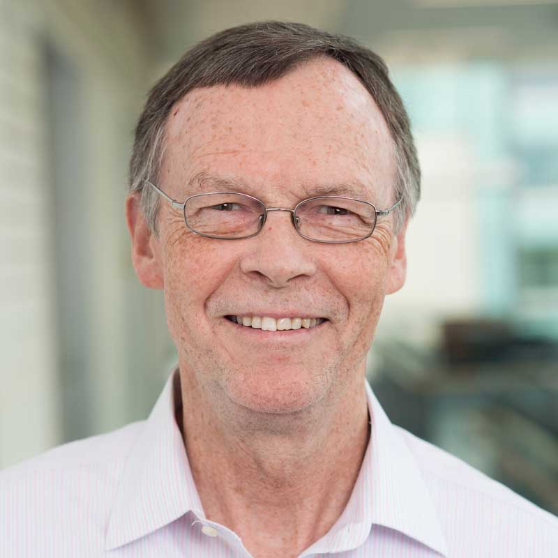Headshot of Bill Tierney smiling, white man wearing pinstriped shirt and wire-rimmed glasses