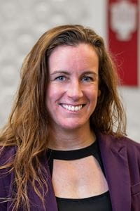 Headshot of Erin Conboy, caucasian woman with long hair, wearing black shirt and purple blazer