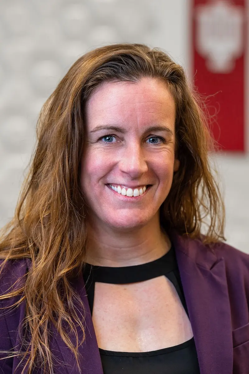 Headshot of Erin Conboy, caucasian woman with long hair, wearing black shirt and purple blazer