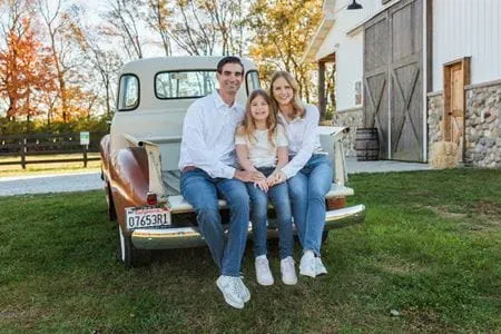 Laura Vater sits in the back of a vintage pickup truck with her husband and daughter, outdoors with fall colors behind