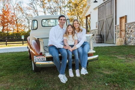 Laura Vater sits in the back of a vintage pickup truck with her husband and daughter, outdoors with fall colors behind