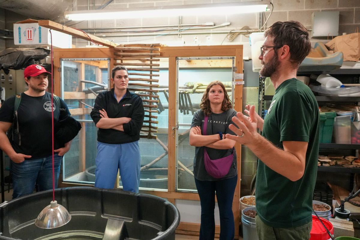 A man wearing a green shirt speaks to medical students at the zoo. 
