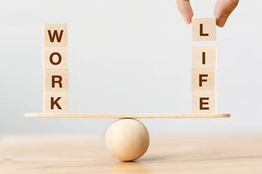 wooden letter tiles spelling "work" and "life" balance on a board held up by a wooden ball