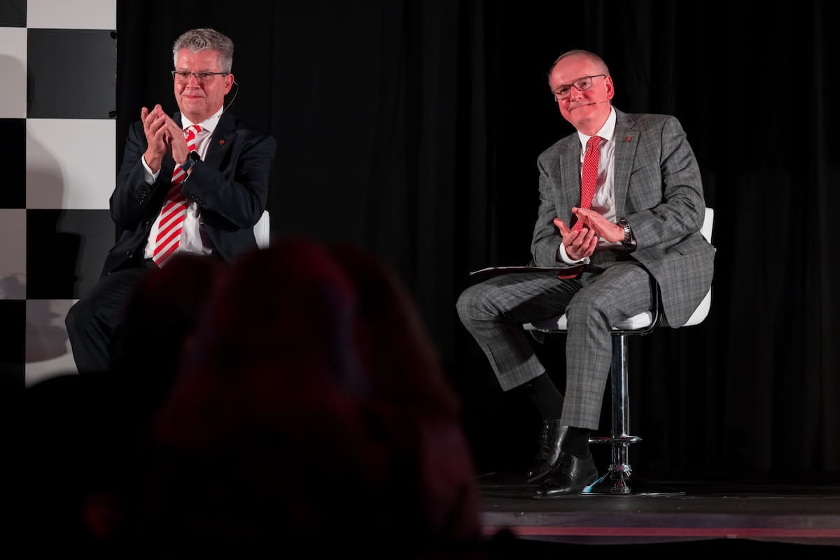 Mark Notestine and Jay Hess sit in chairs on a stage at a fundraising event