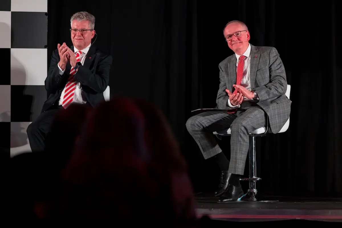 Mark Notestine and Jay Hess sit in chairs on a stage at a fundraising event