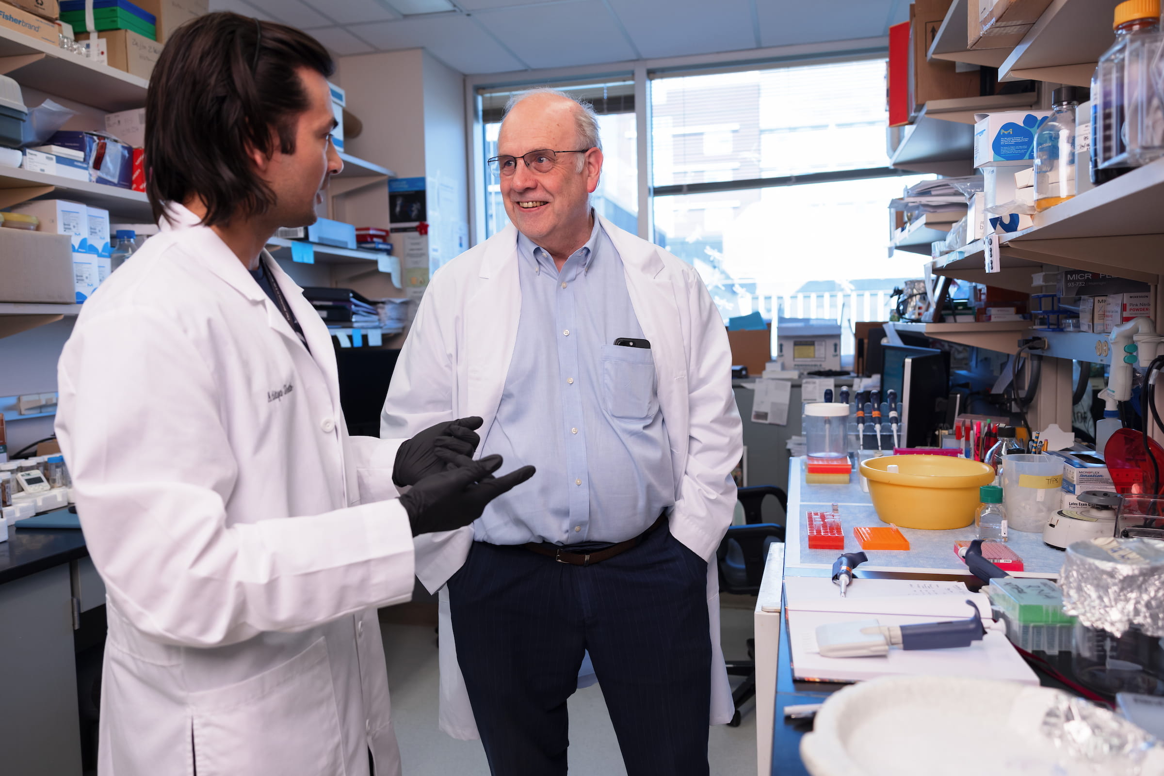 Wade Clapp talks with Aditya Sheth, both wearing lab coats, in a research laboratory
