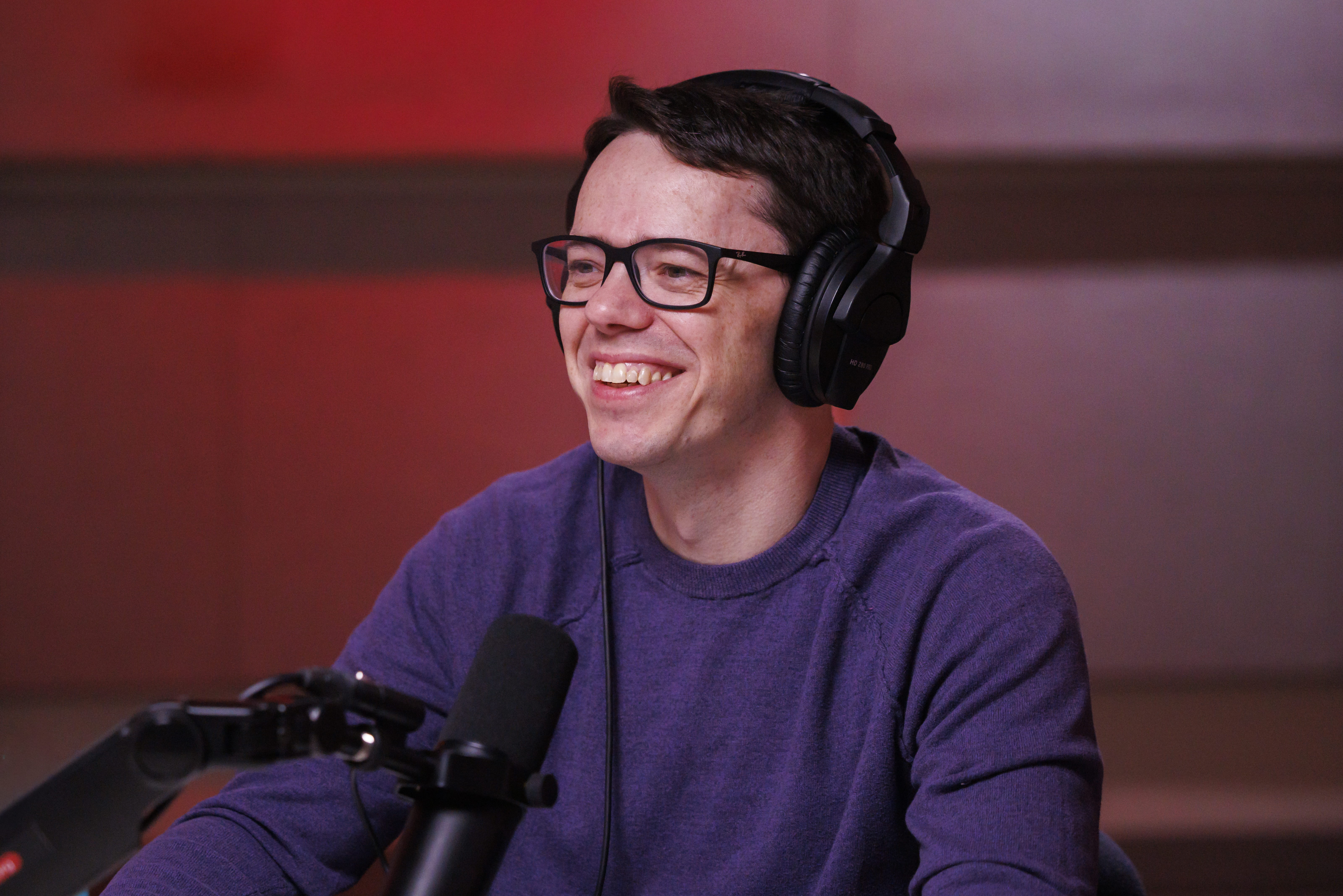 A man wearing glasses and headphones smiles. 