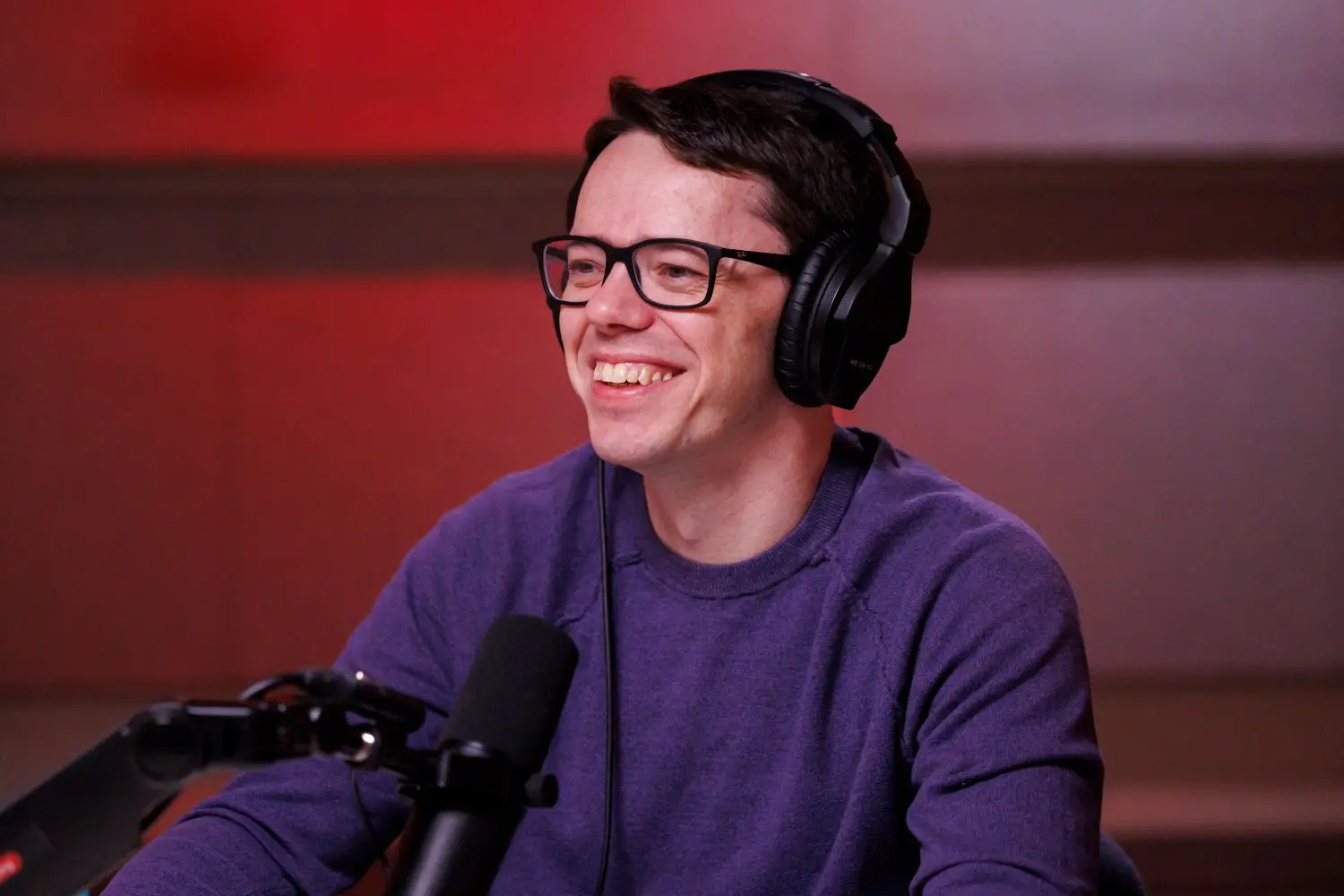 A man wearing glasses and headphones smiles. 