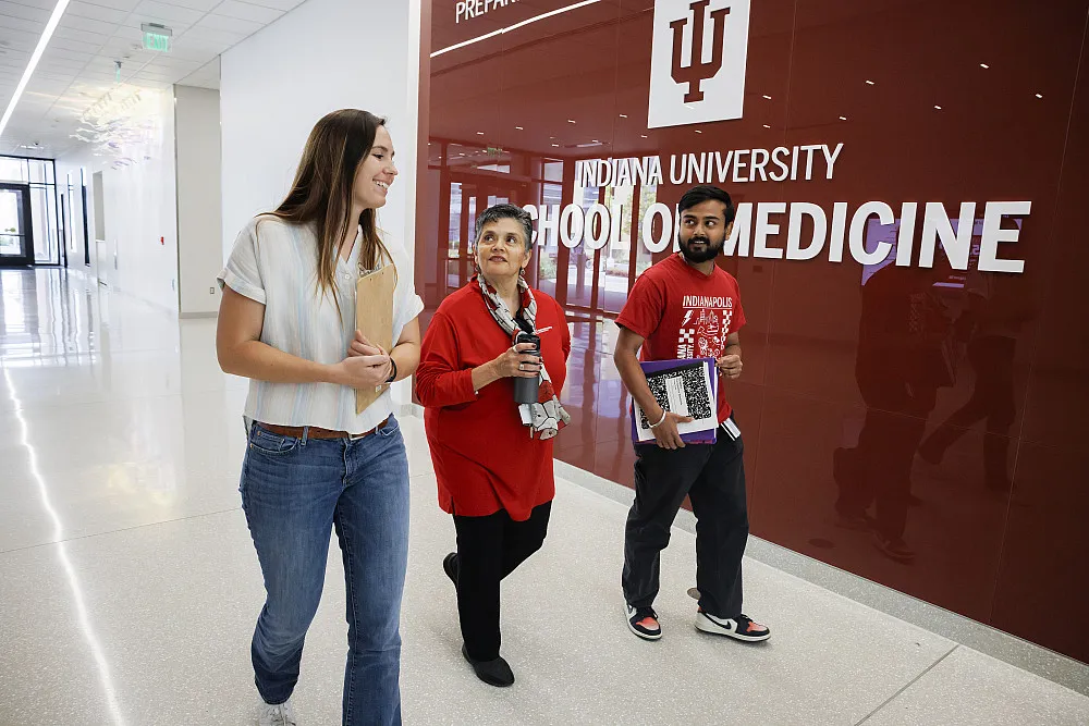 Malú Gámez Tansey speaks with Andrea Merchak and Prithwijit Duttagupta as they walk down a brightly-lit hallway.