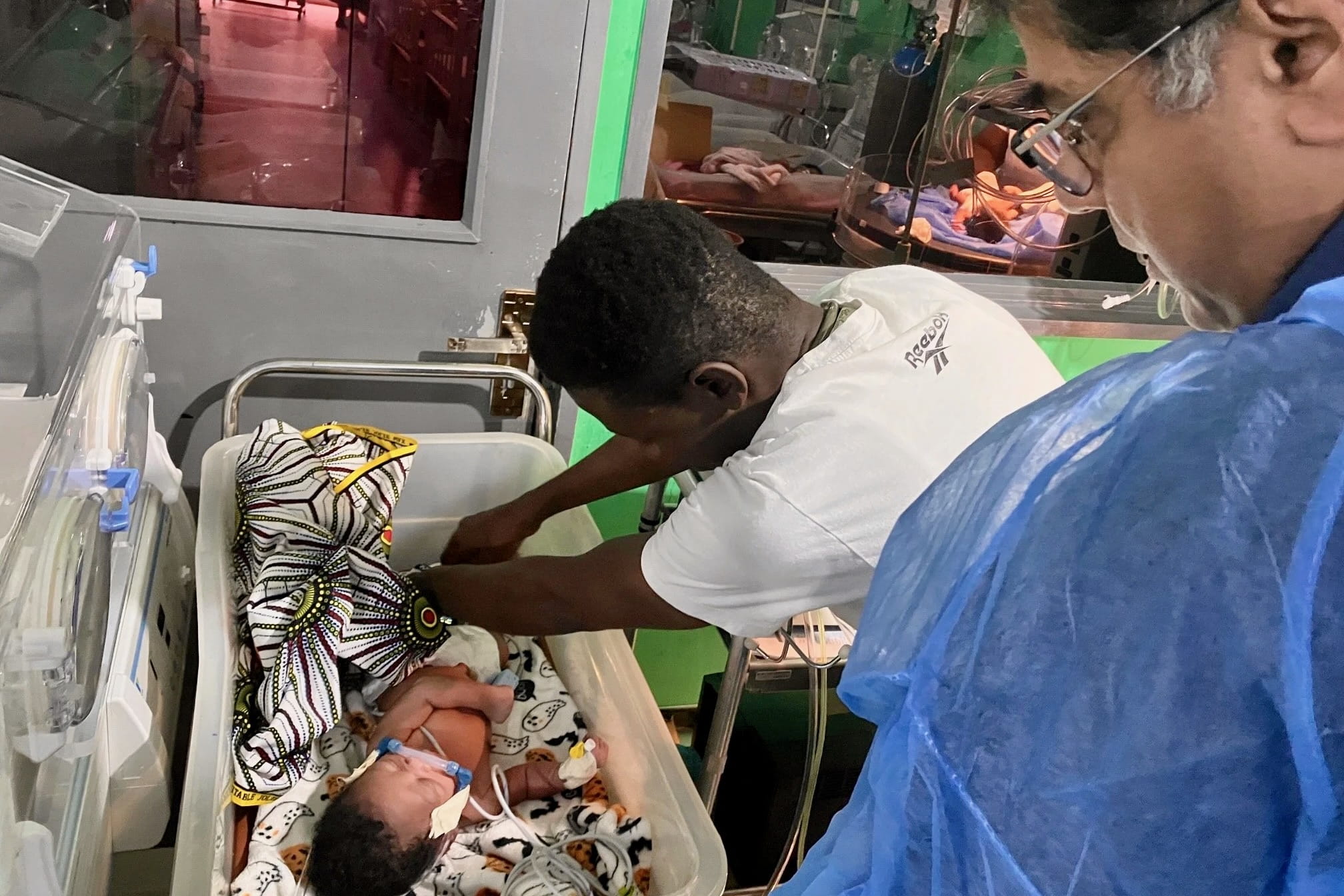 A doctor and a respiratory therapist administer CPAP breathing treatment to a small child in a pediatric intensive care bed in a Liberian hospital.