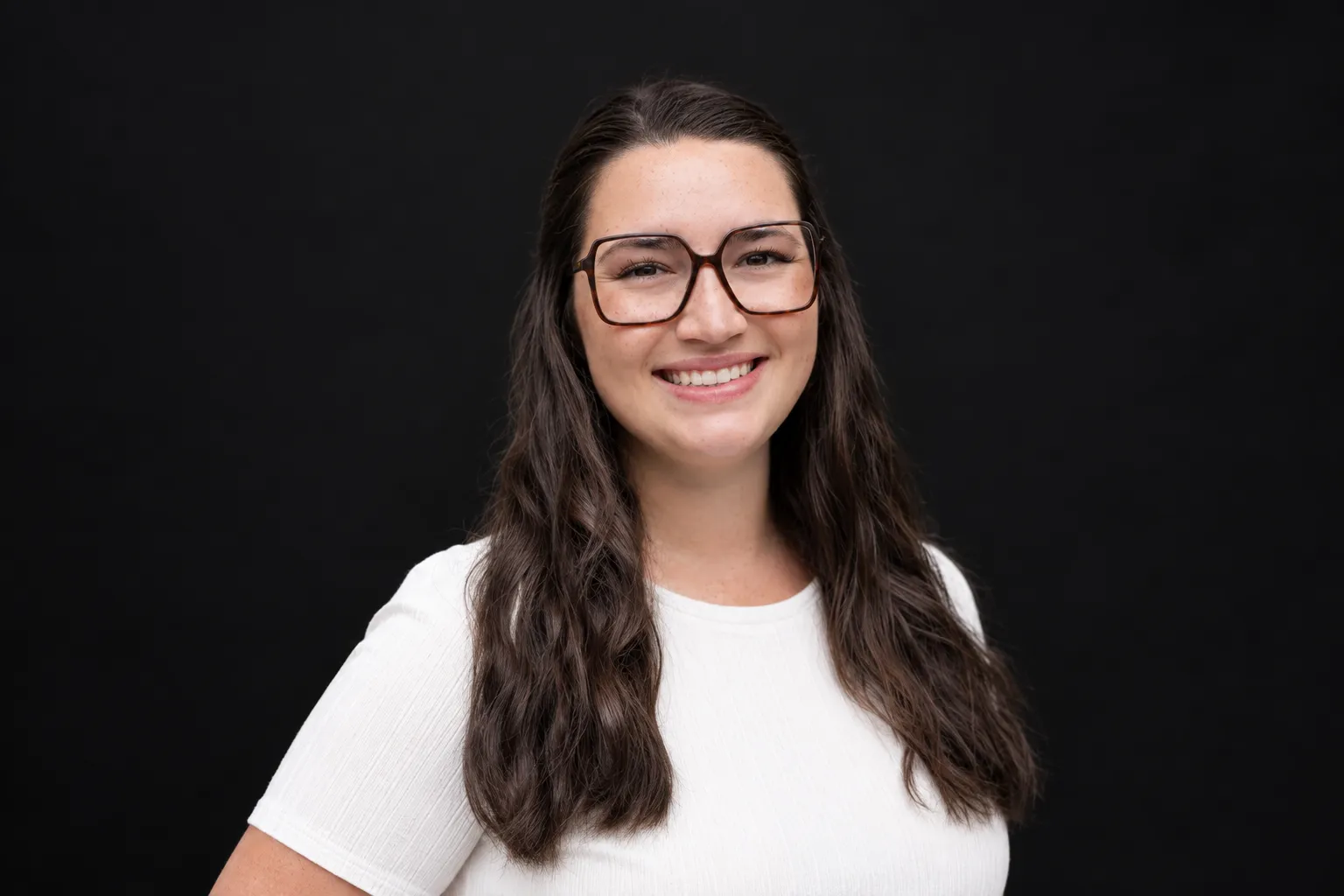 Headshot of Agnes Zybura Wardrop on black background. She is light skinned with long, dark hair and is wearing glasses.
