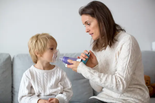 A mother helping her young son administer an inhaler device.