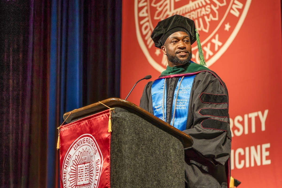Myke Spencer in cap and gown speaking at podium
