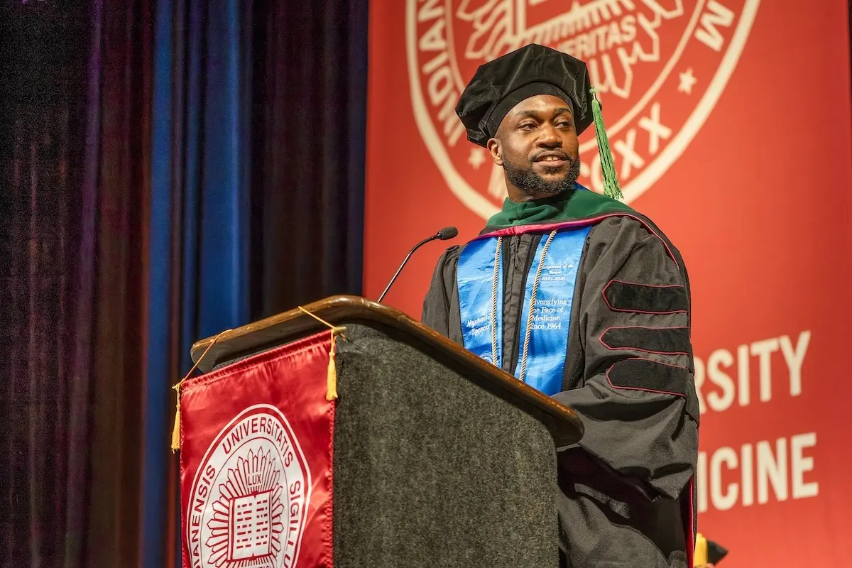 Myke Spencer in cap and gown speaking at podium