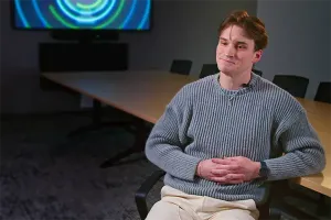 IU medical student Graham Keele sits in a gray sweater in front of a TV display.