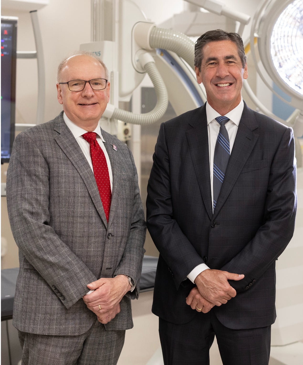 Jay Hess and Dennis Murphy stand in front of clinical equipment wearing suits