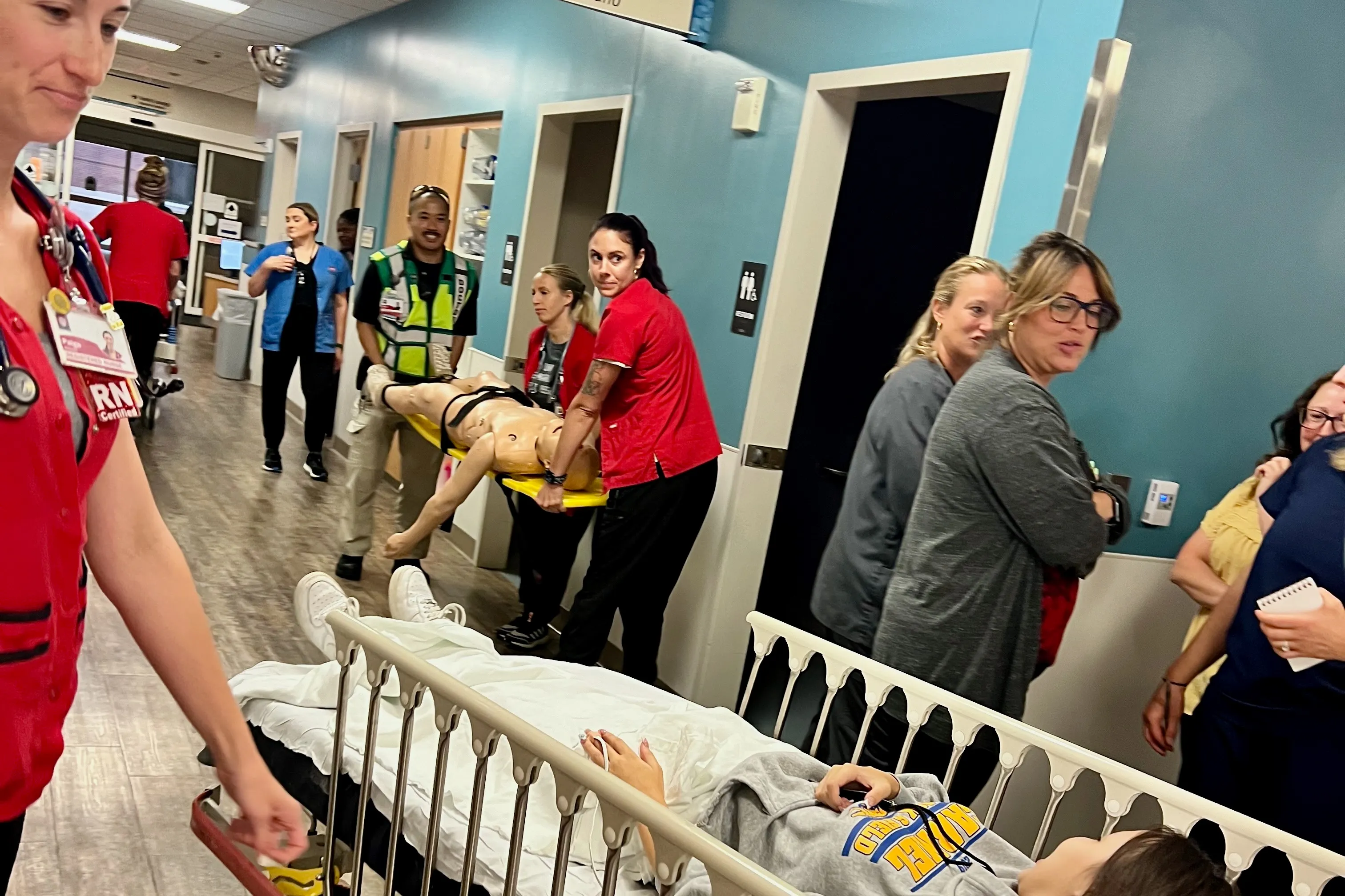 Mark Liao carries a manikin on a stretcher with trainees as other trainees wheel a simulated patient in a bed down a hallway at Riley Hospital for Children during a training exercise.