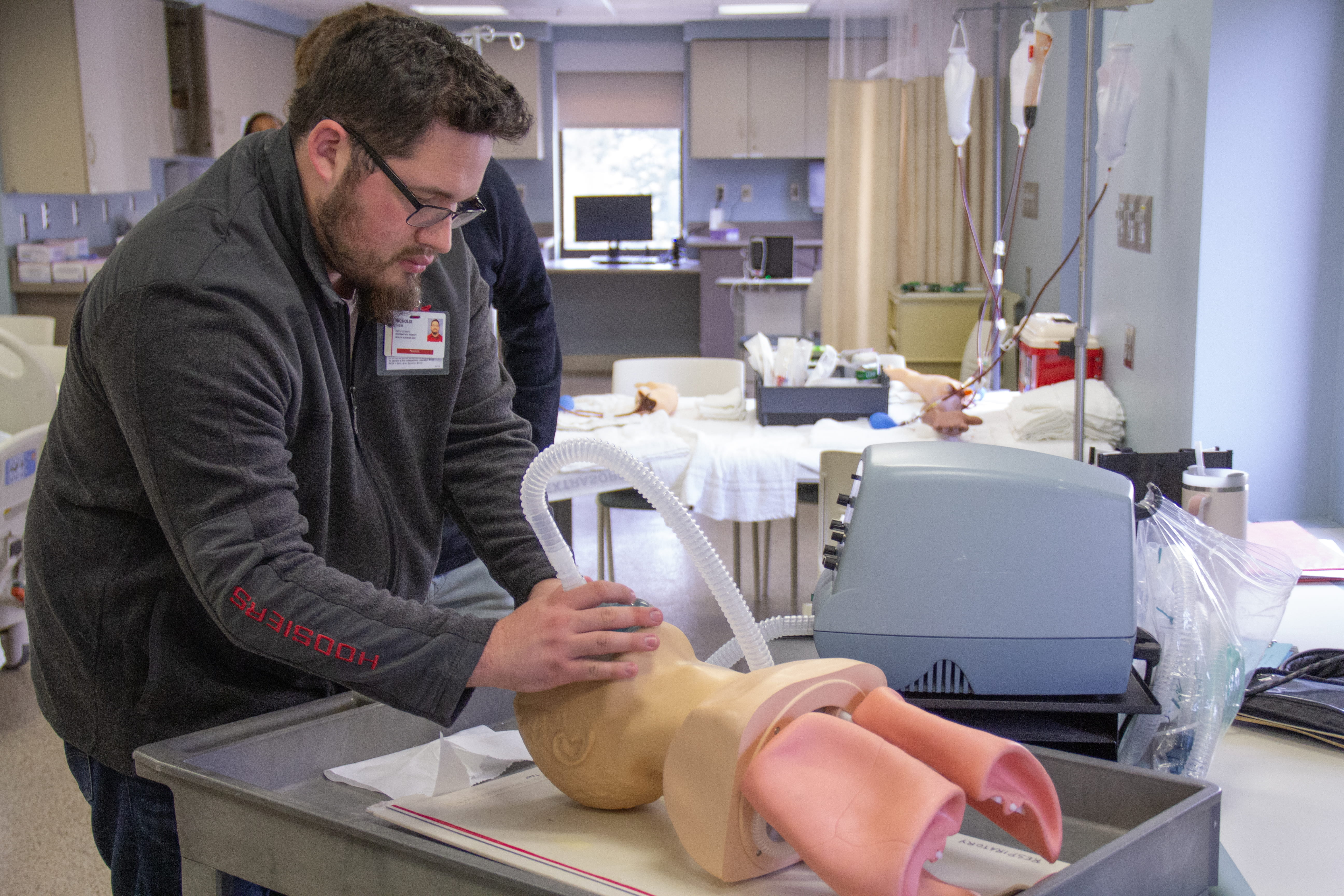 A male student wearing Hoosiers apparel practices giving oxygen to a manikin in a clinical setting. 