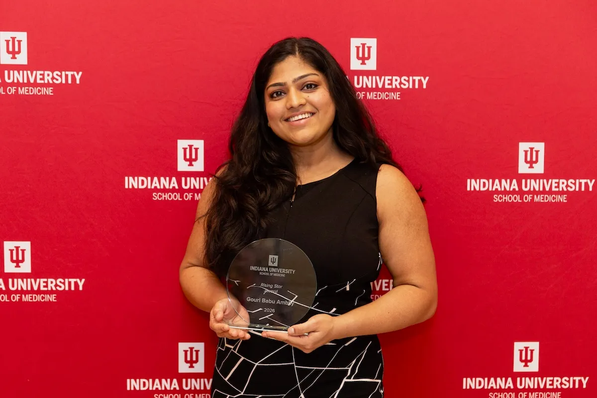 Gouri Babu Ambily holds her award as she poses in front of a red IU School of Medicine backdrop.