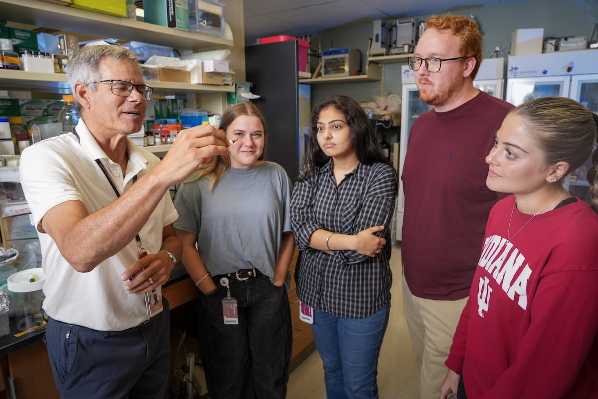 John Turchi holds a test tube while talking to members of his lab, gathered around him