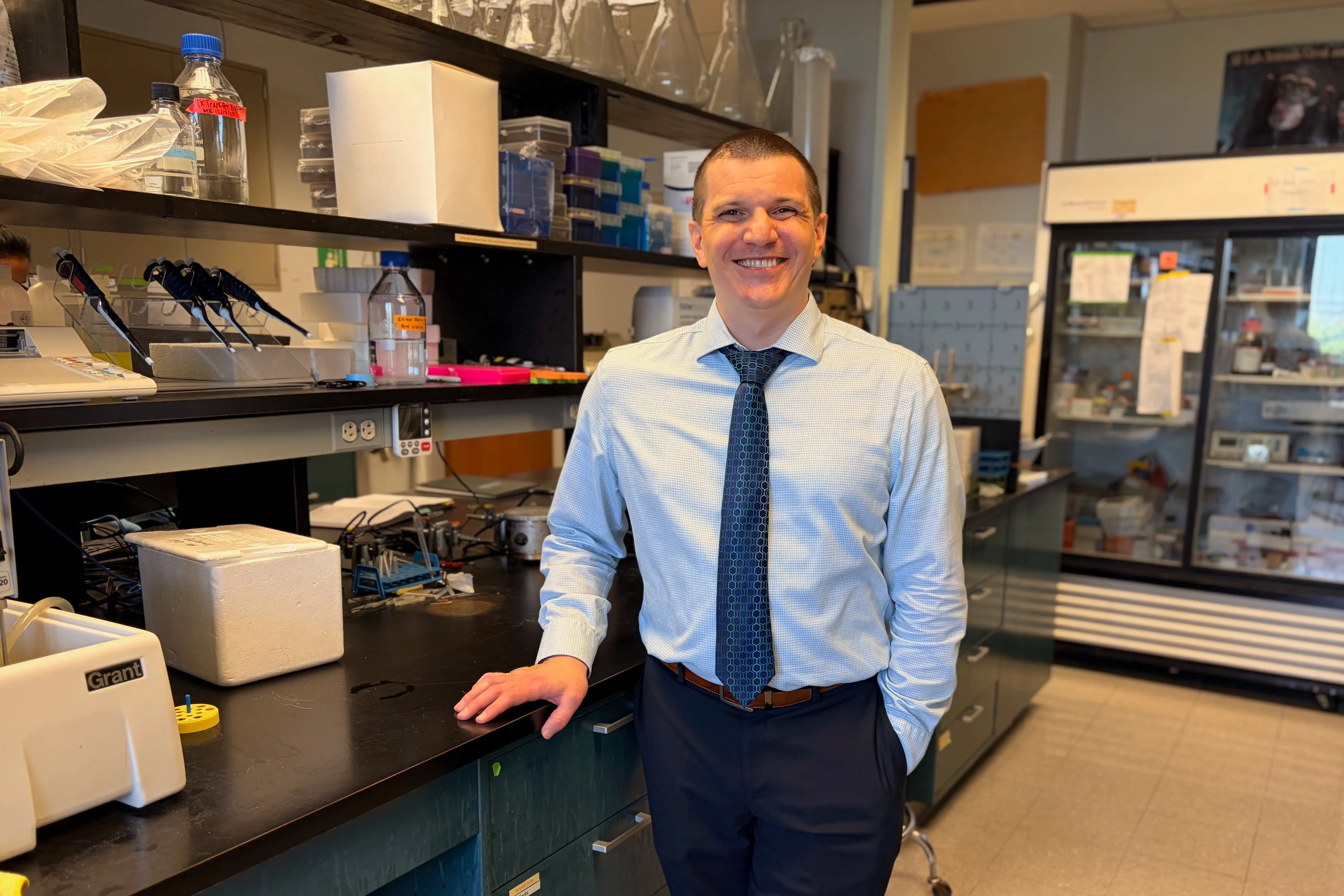 Kyle Gospodarek stands in a lab at the IU Hydrocephalus Research Center. He is wearing a blue shirt and tie and has a short buzzcut.