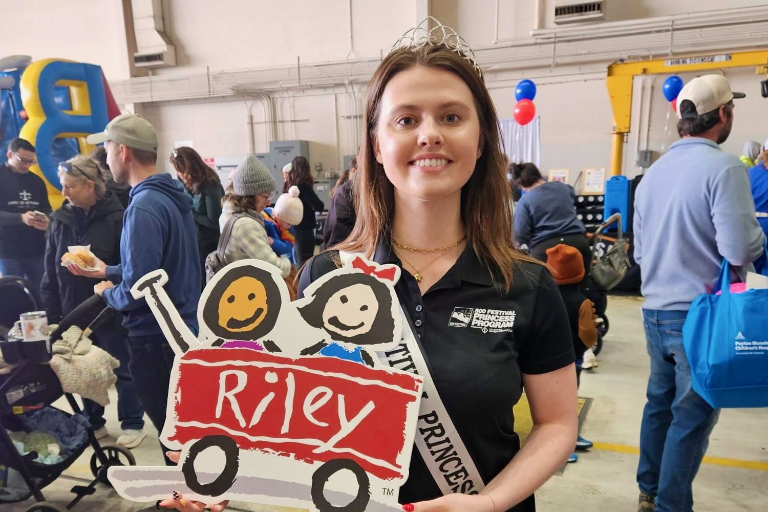 Lilly O'Shea wears a princess tiara and holds a Riley red wagon sign during a 500 Festival event