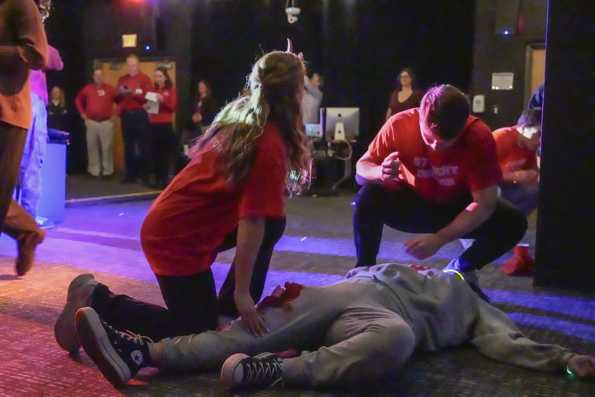 Medical students assess the condition of an actor with a leg injury during a mass casualty simulation in a low light room with instructors observing