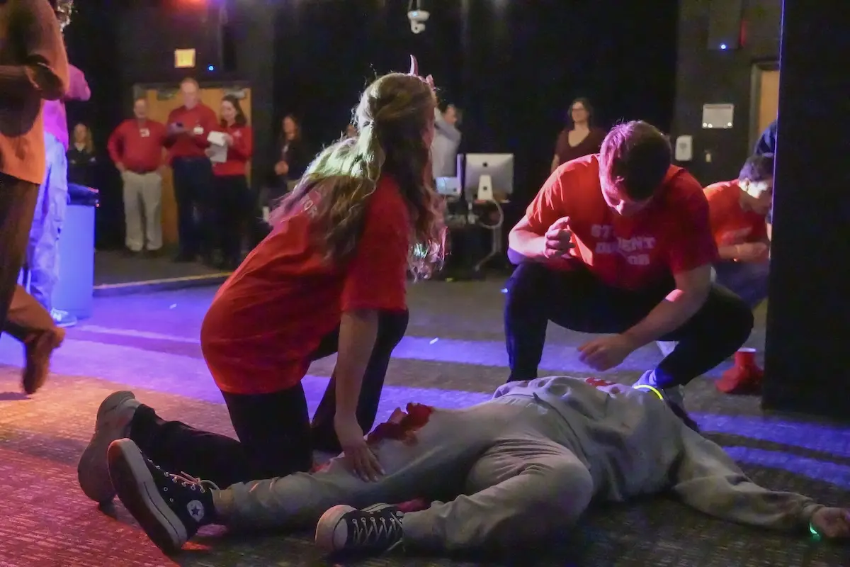 Medical students assess the condition of an actor with a leg injury during a mass casualty simulation in a low light room with instructors observing