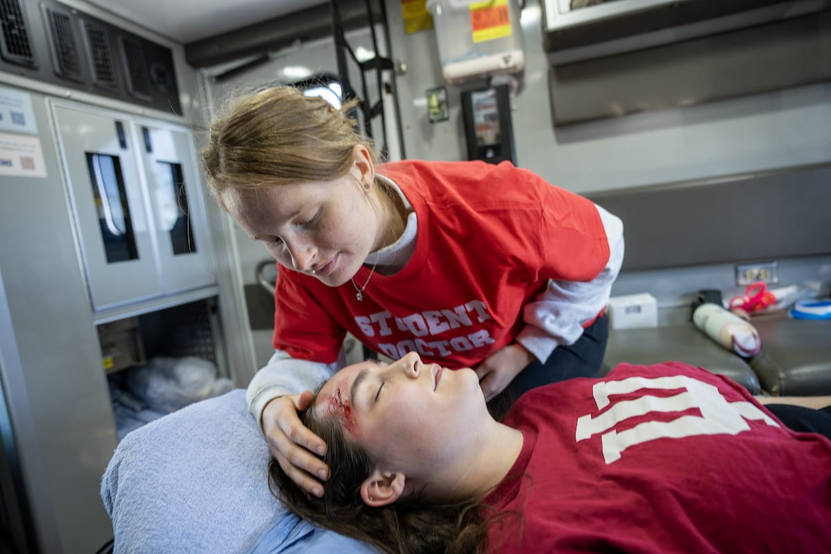 A medical student inspects a head wound of a patient in an ambulance