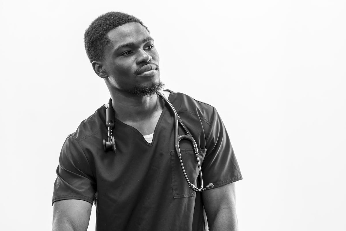Black-and-white portrait of Mout-Maine Moustapha in scrubs with a stethoscope around his neck.