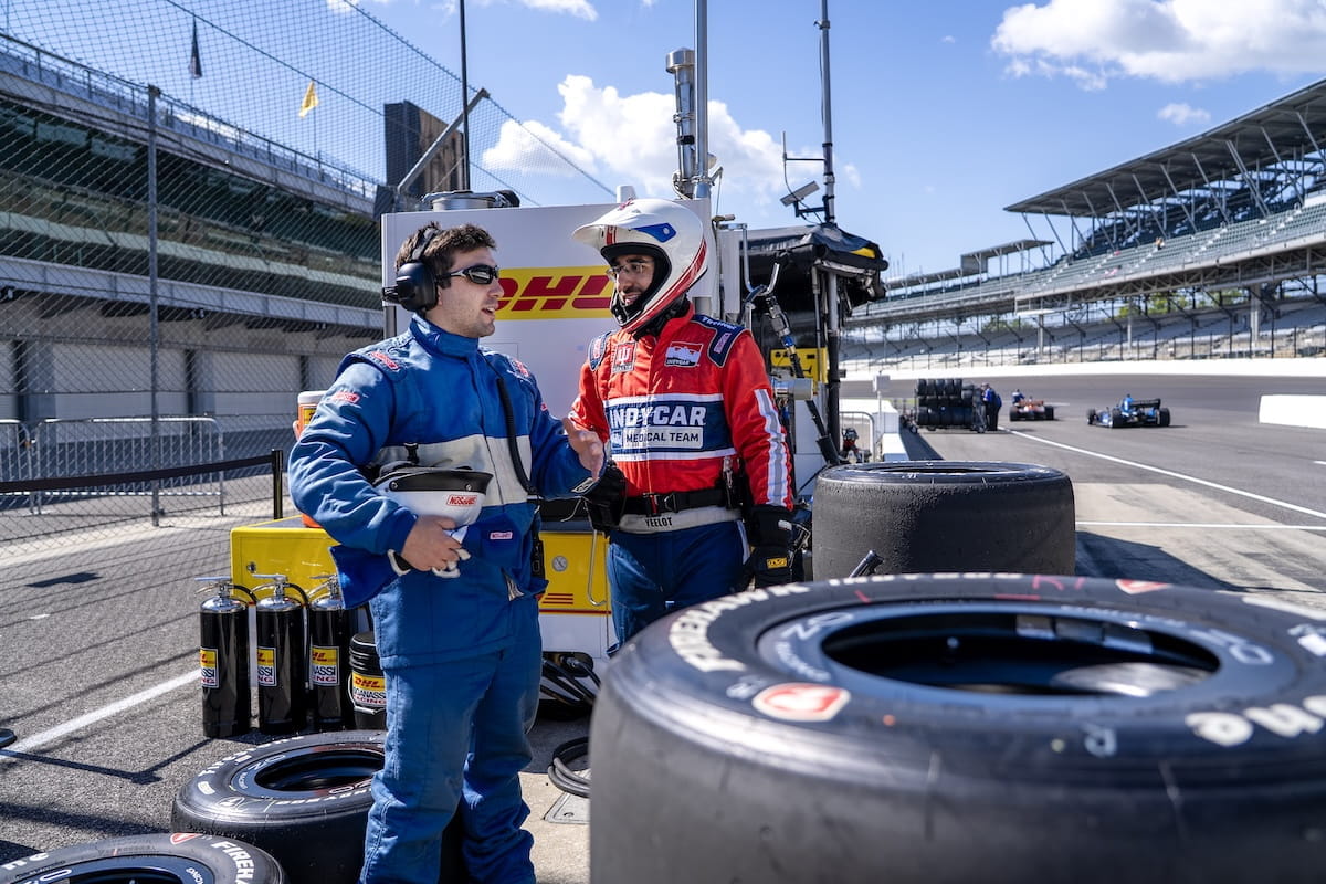 Two men in fire suits talk near stacked tires on pit lane at the Indianapolis Motor Speedway