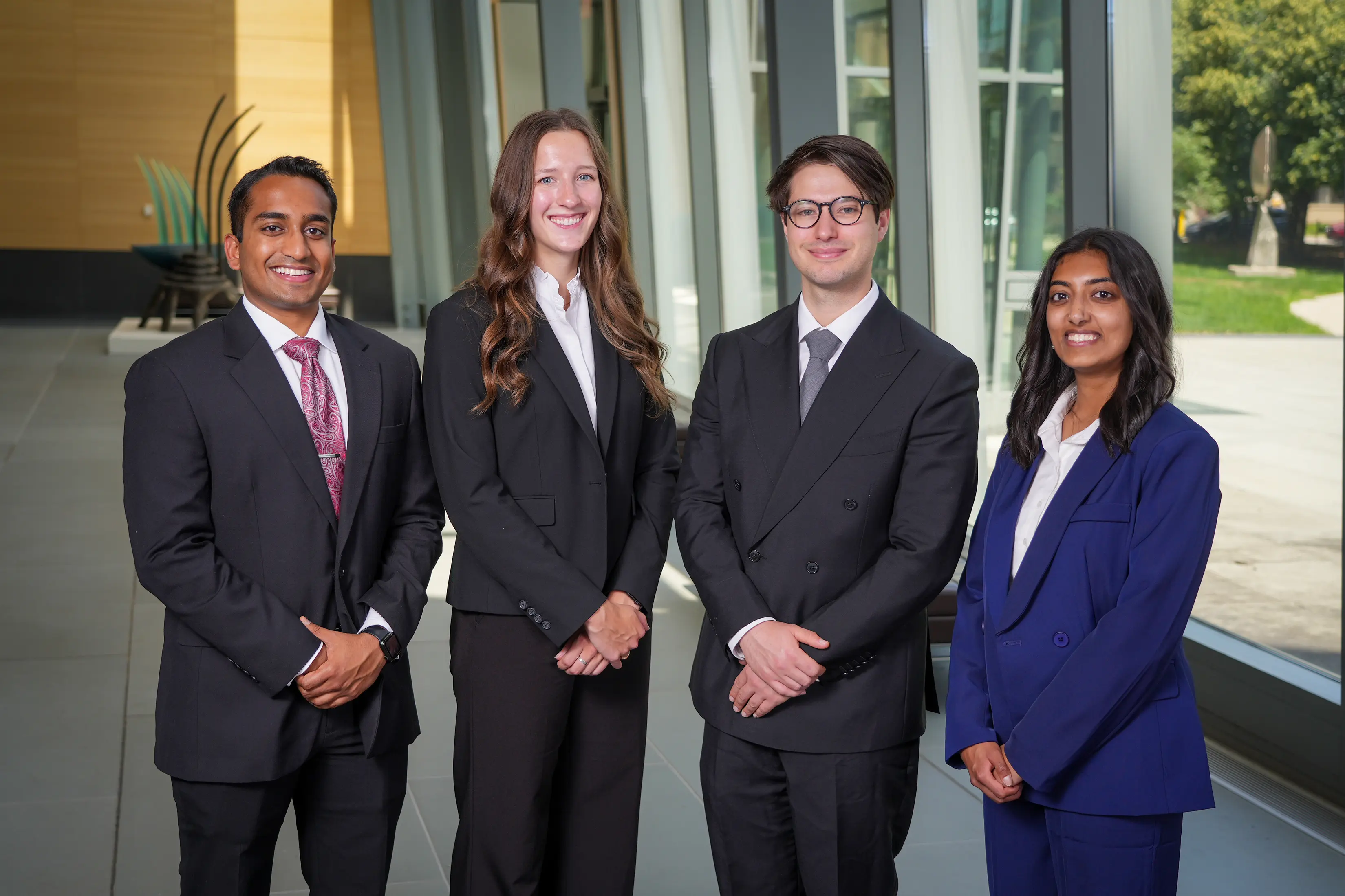  Four people in business attire standing together in a bright hospital or academic medical center lobby.
