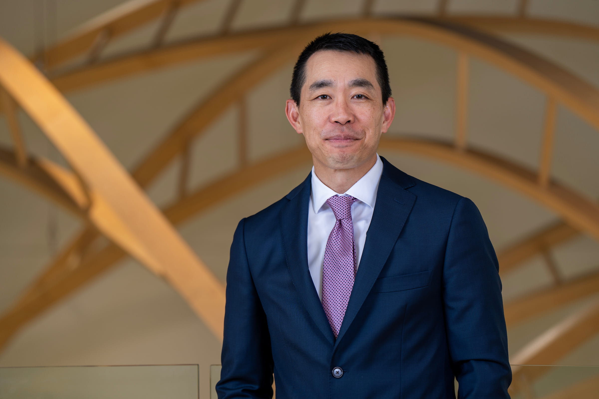 Peter Pang stands in front of a double helix, wearing a navy suit and purple tie