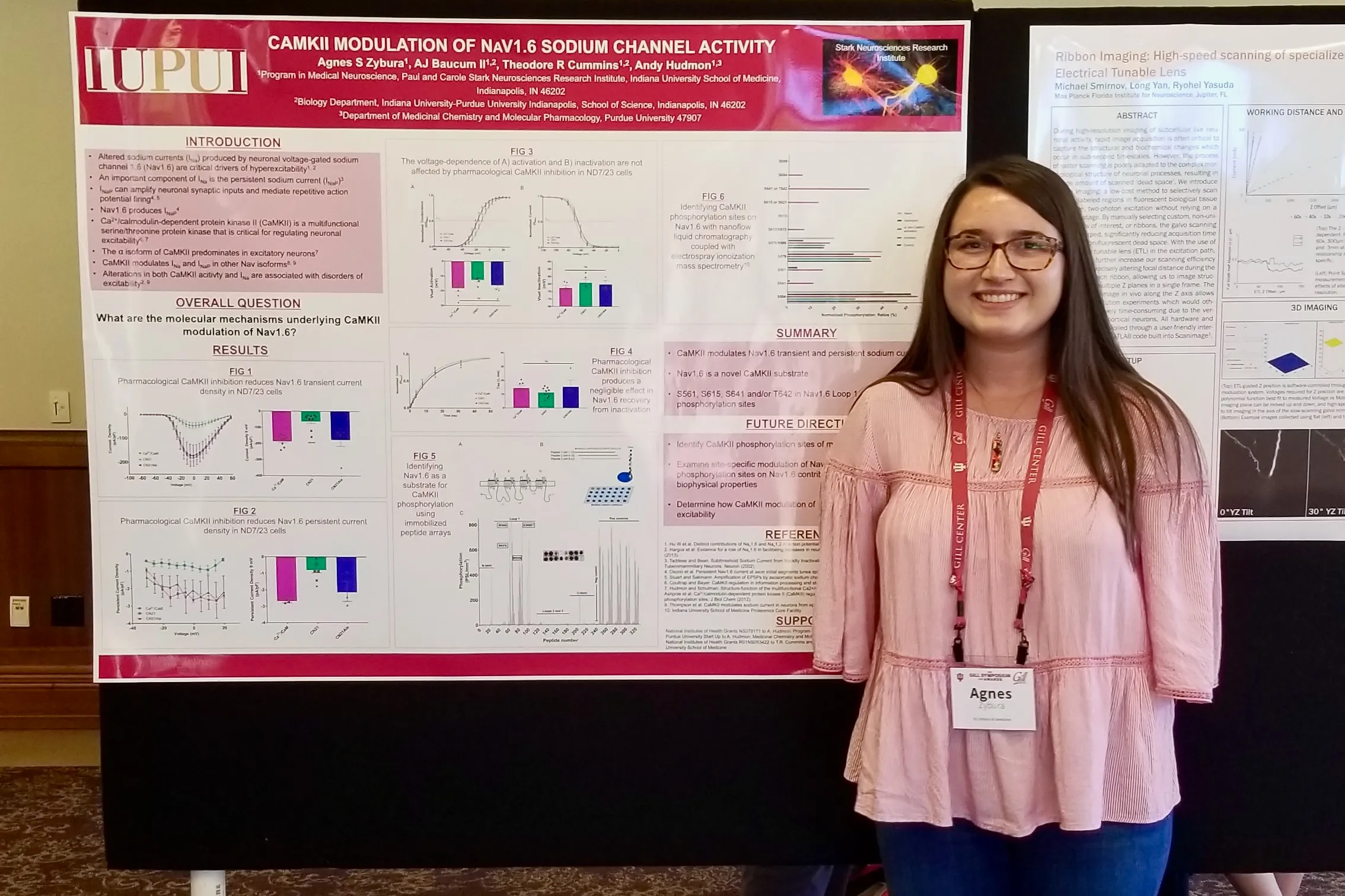 Agnes Zybura Wardrop, wearing a pink top, stands in front of a large poster presentation of her PhD research. 