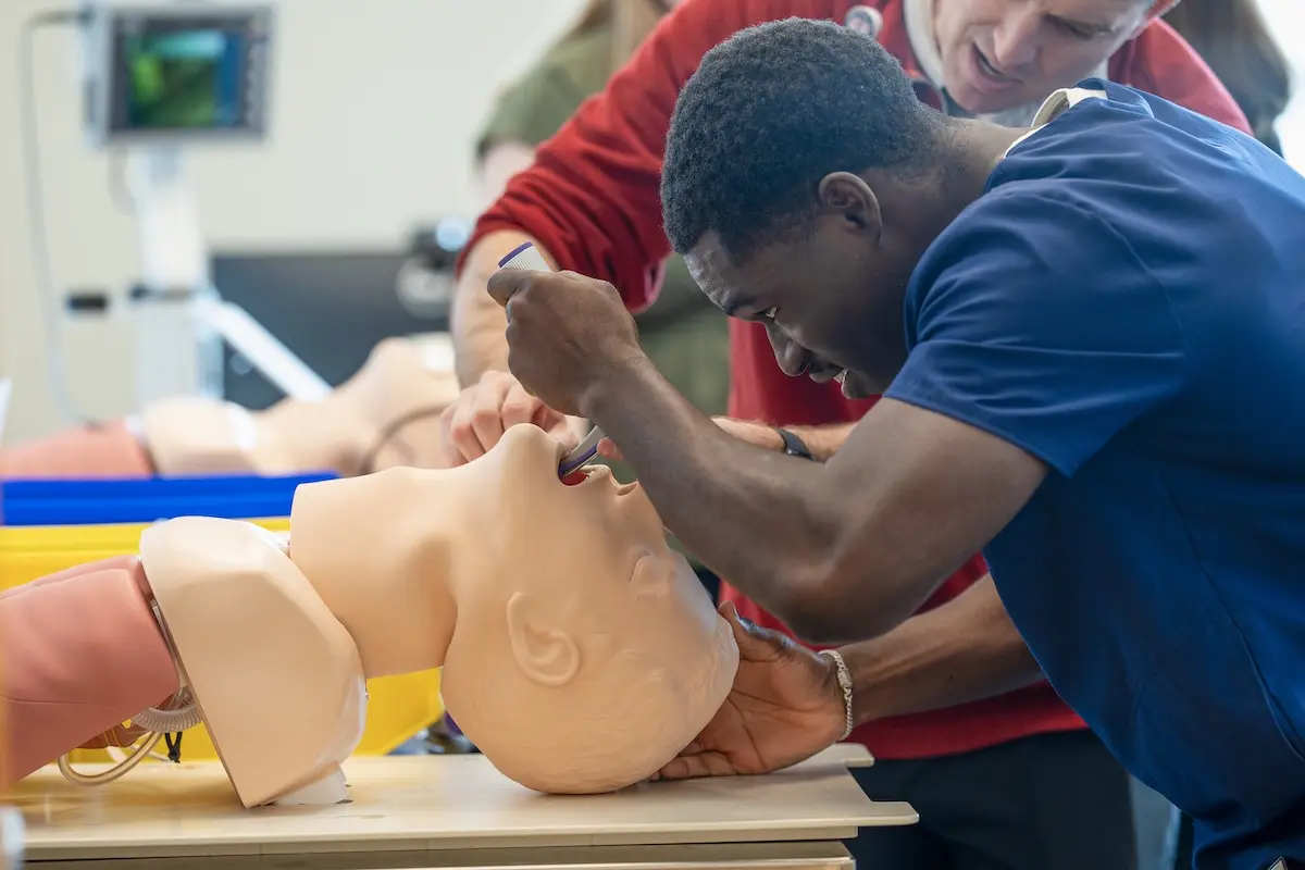 Maine Moustapha practices intubation on a manikin as an instructor assists.
