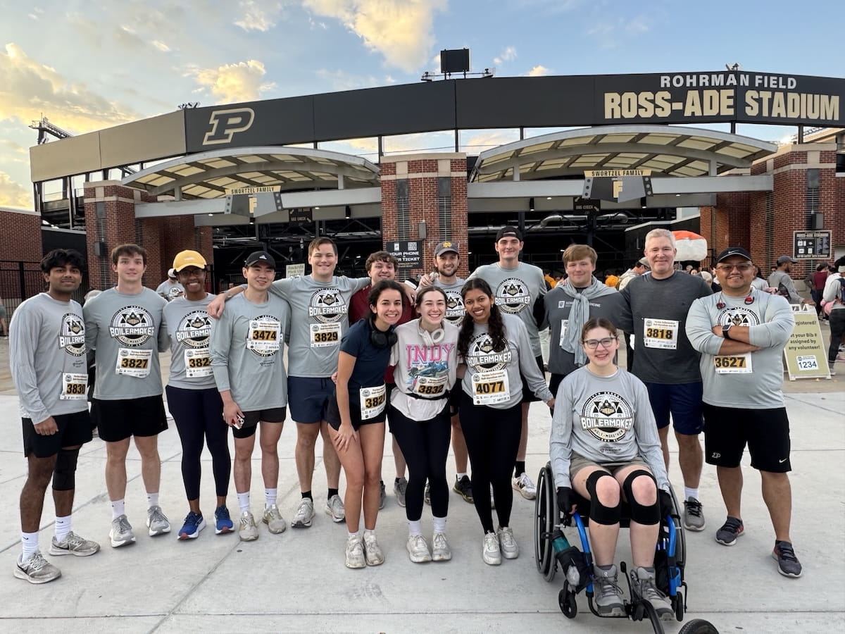 Sarah Vaught sits in her wheelchair with a group of her peers standing behind her, all wearing Purdue 5K T-shirts