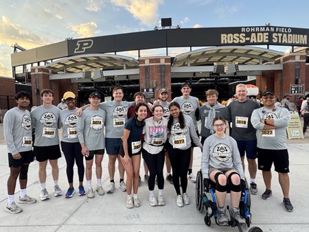 Sarah Vaught sits in her wheelchair with a group of her peers standing behind her, all wearing Purdue 5K T-shirts