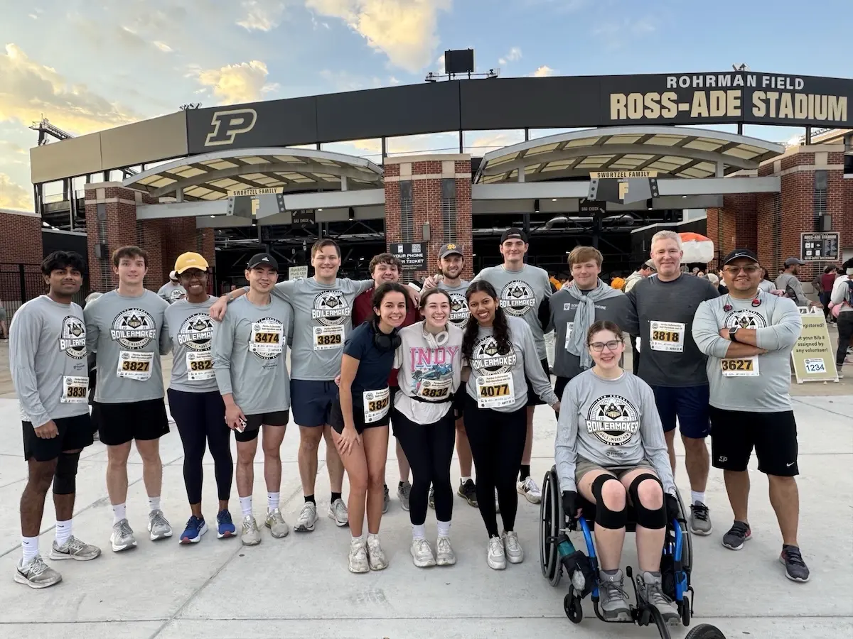 Sarah Vaught sits in her wheelchair with a group of her peers standing behind her, all wearing Purdue 5K T-shirts