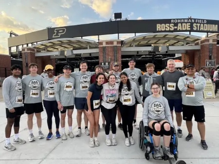 Sarah Vaught sits in her wheelchair with a group of her peers standing behind her, all wearing Purdue 5K T-shirts