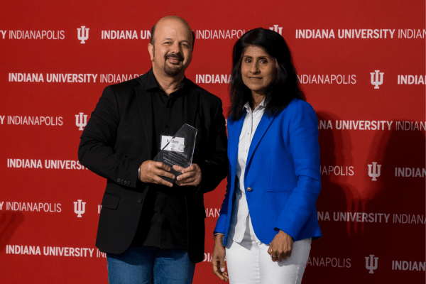 Reuben Kapur poses with an award next to IU Indianapolis Chancellor Latha Ramchand, against an IU Indianapolis-branded back drop.