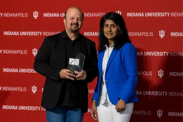 Reuben Kapur poses with an award next to IU Indianapolis Chancellor Latha Ramchand, against an IU Indianapolis-branded back drop.