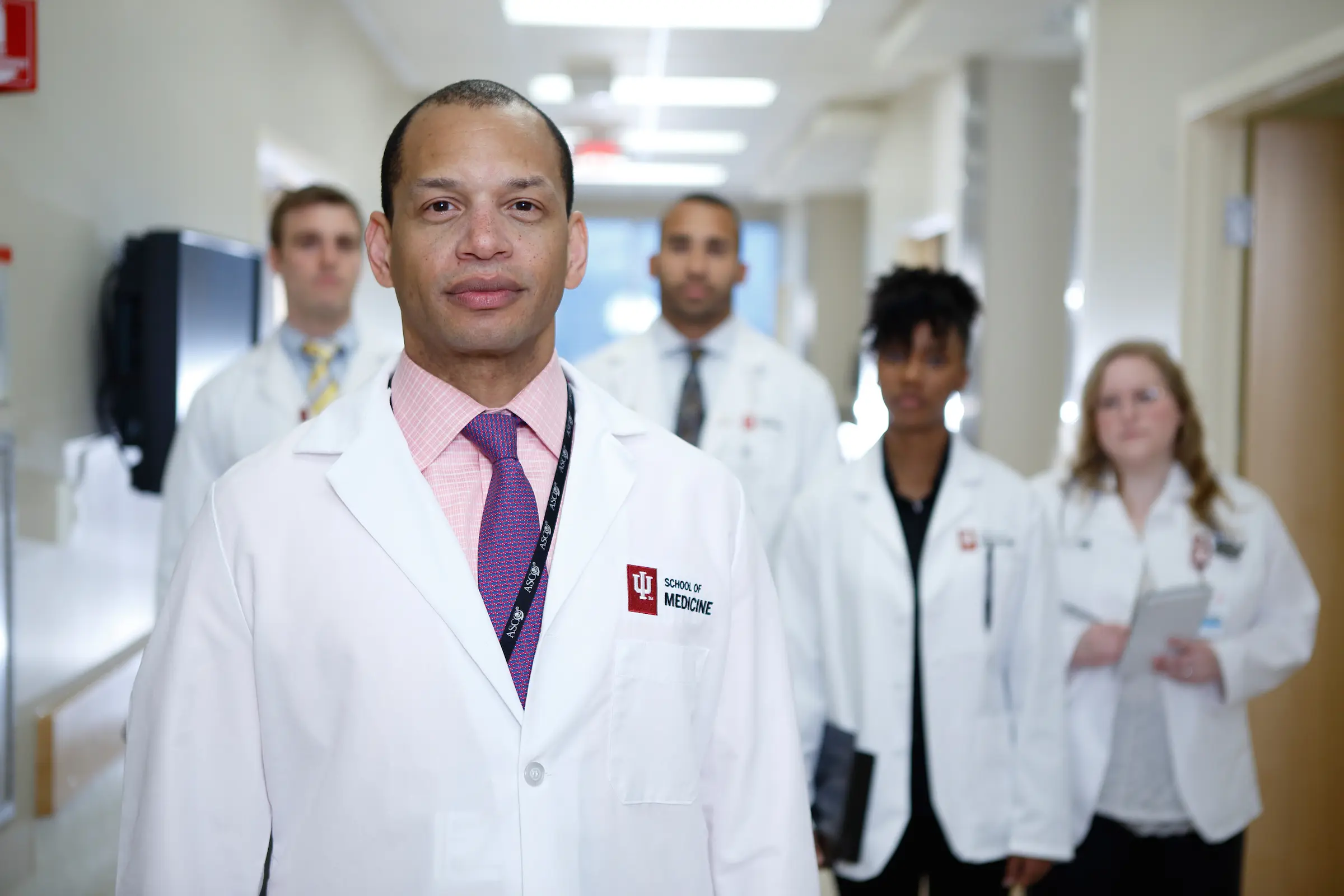 Dr. Rich Zellars stands in front of four other doctors in a hospital hallway. All are wearing white coats.