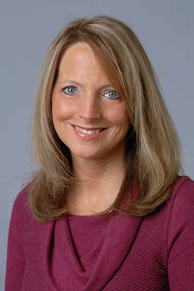 Professional headshot of a woman with straight blonde hair, smiling, wearing a maroon top, photographed against a plain gray background. Photo/Image courtesy: Stephanie Sharpe