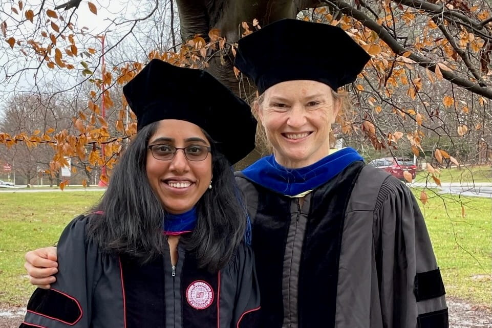 Graduate Shruthi Sriramkumar and Dr. O'Hagan pose in their graduation regalia outdoors on a fall day.